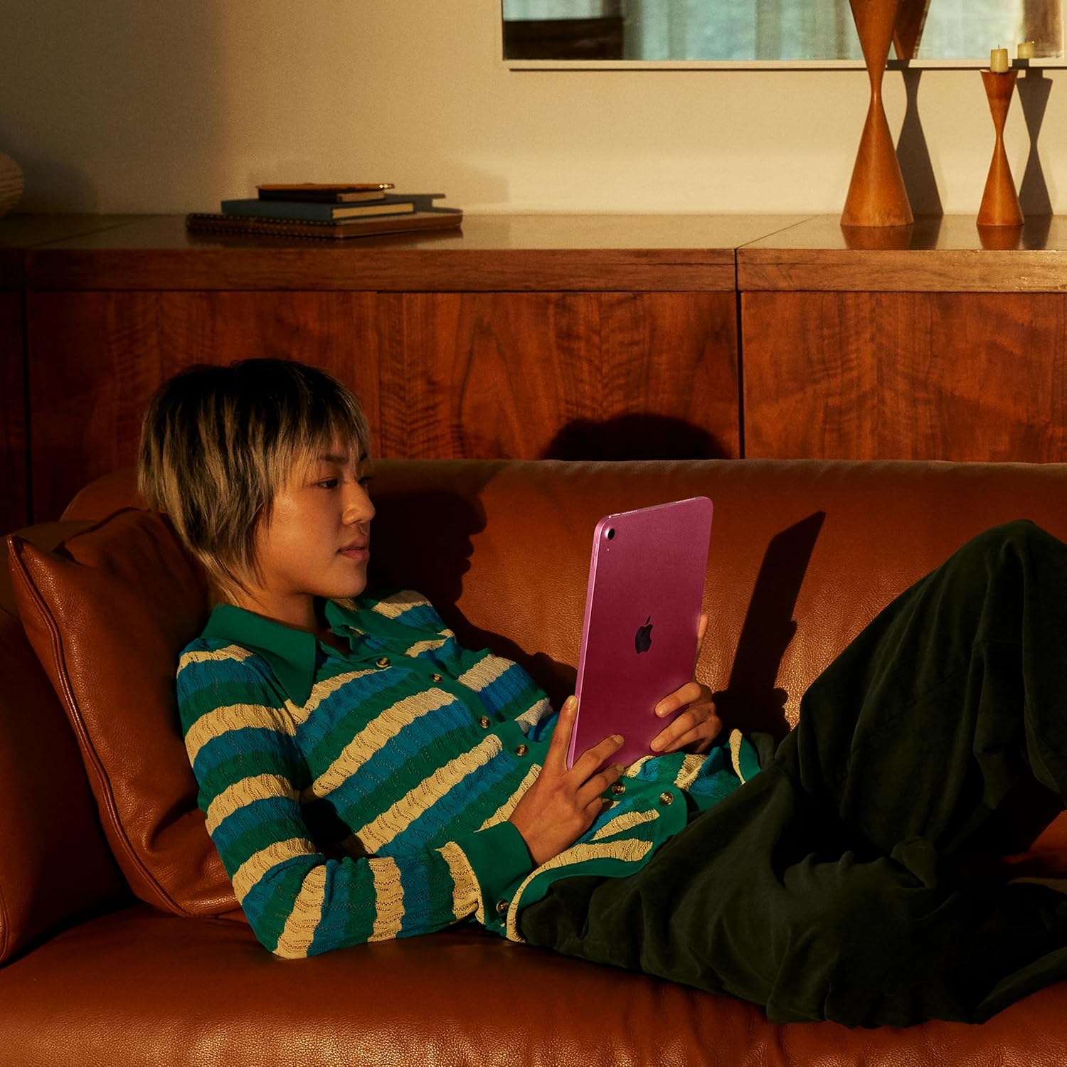 Person sitting on a couch using a pink tablet in a warm, dimly lit room.