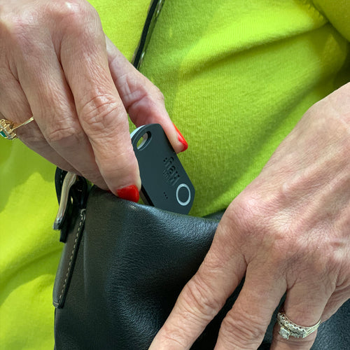 Person holding a black electronic device next to a green jacket