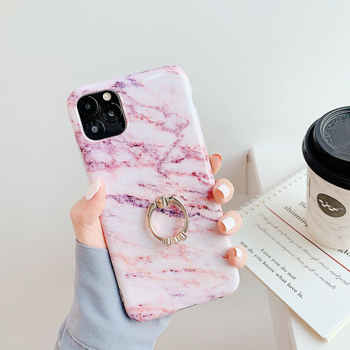 Phone case with marble pattern and ring holder held by a hand, with a coffee cup and book in the background.